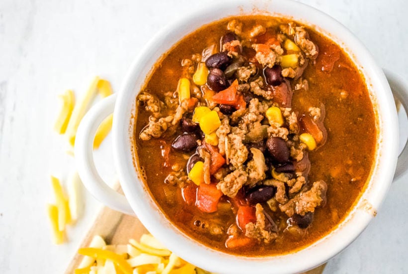 Top view of white bowl filled with ground beef taco soup with shredded cheese on the side.