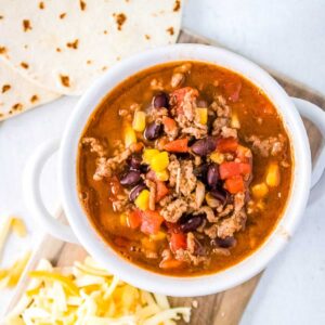 Top view of a white bowl filled with simple taco soup with shredded cheese and tortillas on the side.