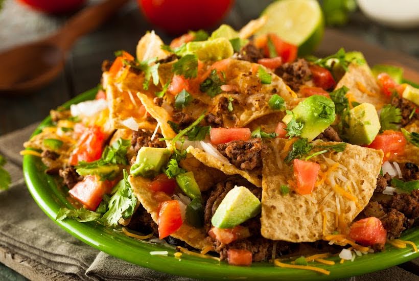 Platter of nachos garnished with avocado, tomato and cilantro.