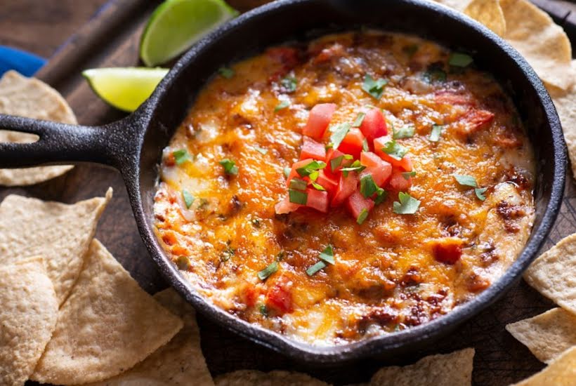 Cast iron skillet of cheesy dip with chopped tomatoes and tortilla chips.