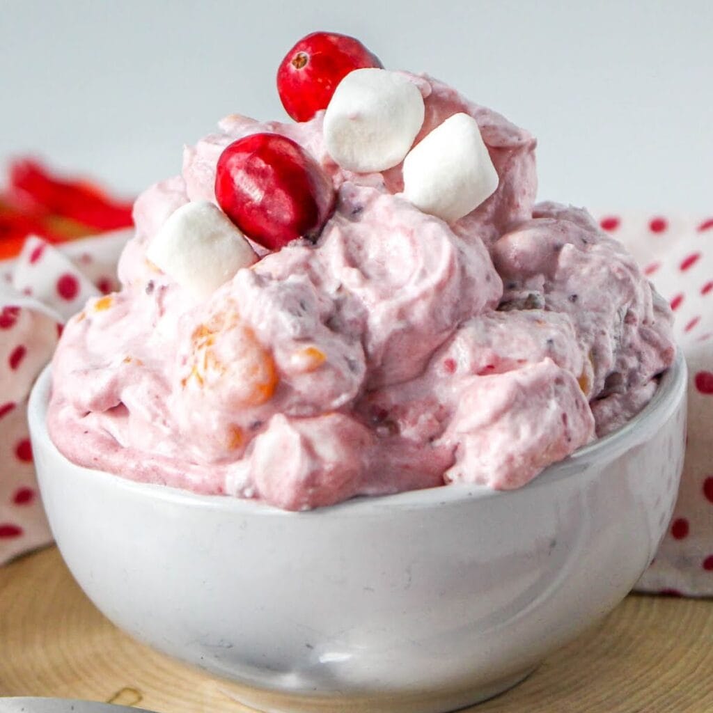 Closeup of a white bowl filled with cranberry fluff with oranges and garnished with marshmallows and fresh cranberries.