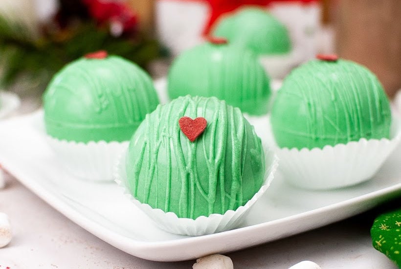 Front view of Grinch-themed hot chocolate bombs on a white plate.